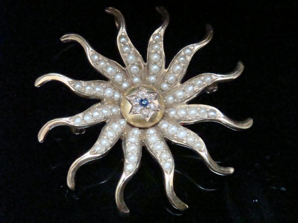 An antique 14ct yellow gold starburst pendant brooch decorated with seed pearl rays around a central star setting with a sapphire and rose-cut diamonds. View VIII