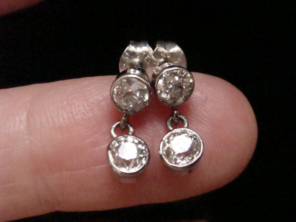 Pair of Edwardian 18ct white gold drop earrings featuring rubover bezel-set old cut diamonds. View III