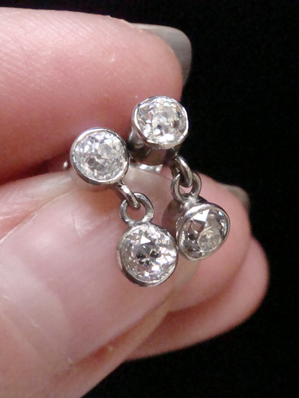 Pair of Edwardian 18ct white gold drop earrings featuring rubover bezel-set old cut diamonds. View IV