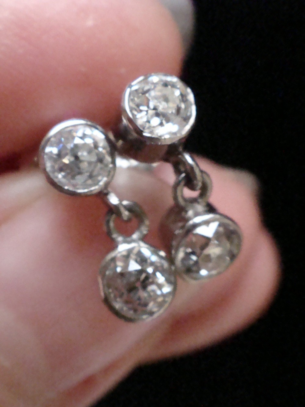 Pair of Edwardian 18ct white gold drop earrings featuring rubover bezel-set old cut diamonds. View V