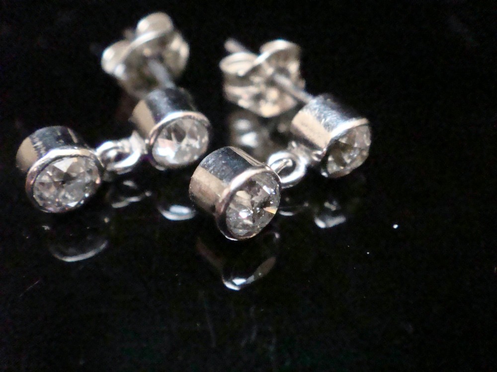 Pair of Edwardian 18ct white gold drop earrings featuring rubover bezel-set old cut diamonds. View VII