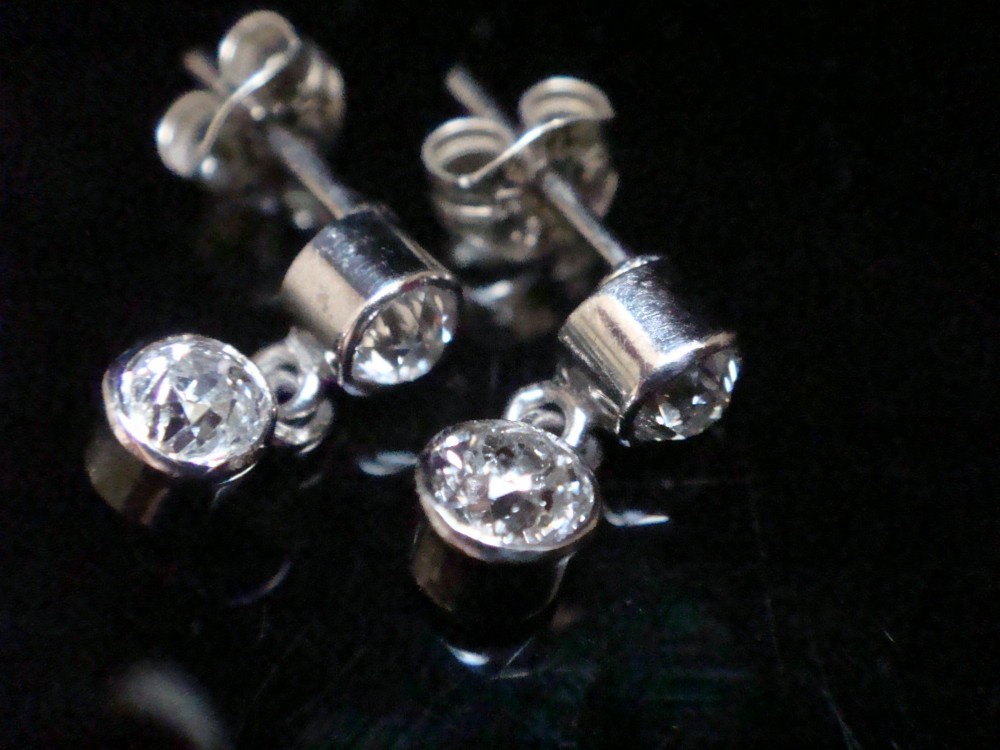 Pair of Edwardian 18ct white gold drop earrings featuring rubover bezel-set old cut diamonds.