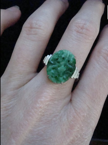 An Art Deco platinum ring featuring a carved oval imperial green jadeite gemstone set with stepped geometric shoulders. View V