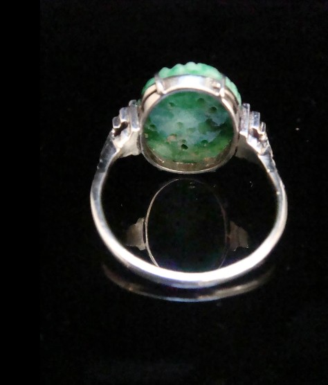 An Art Deco platinum ring featuring a carved oval imperial green jadeite gemstone set with stepped geometric shoulders. View VI