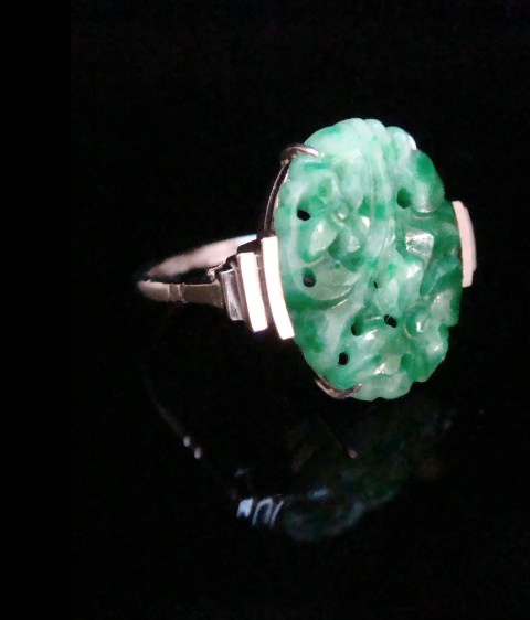 An Art Deco platinum ring featuring a carved oval imperial green jadeite gemstone set with stepped geometric shoulders. View VII