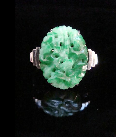 An Art Deco platinum ring featuring a carved oval imperial green jadeite gemstone set with stepped geometric shoulders.