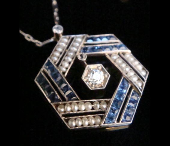 An Edwardian hexagonal platinum pendant featuring calibre-cut blue sapphires, natural seed pearls, and a centre diamond on a fine chain. View II