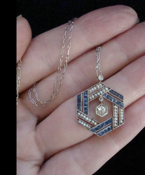 An Edwardian hexagonal platinum pendant featuring calibre-cut blue sapphires, natural seed pearls, and a centre diamond on a fine chain. View III