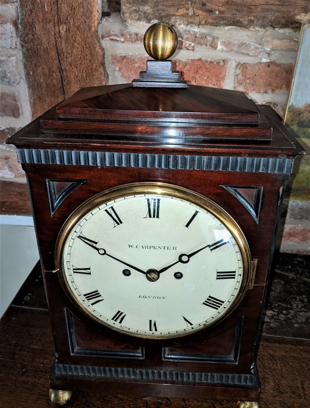 A 19th-century mahogany fusee bracket clock with a brass finial, brass ball feet, fluted wood trim, and a white dial displaying Roman numerals. View V