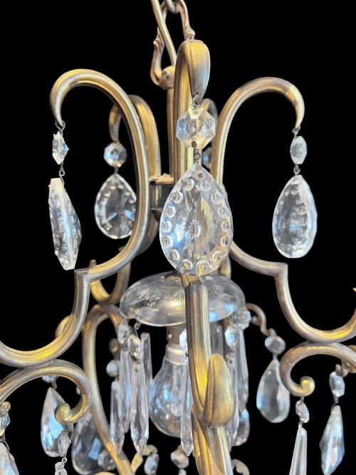 fig 1. A single-light ceiling chandelier featuring a curved brass frame suspended with clear faceted crystal teardrop pendants.