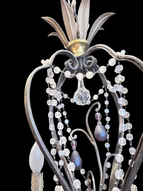 fig 2. A four-arm French antique chandelier featuring a dark metal cage frame adorned with clear and amethyst-tinted glass crystal beads and teardrop pendants.