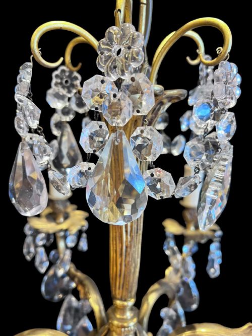 fig 1. A six-light French ormolu ceiling chandelier decorated with clear faceted crystal drops, candle-shaped light sockets, and a central fluted column.