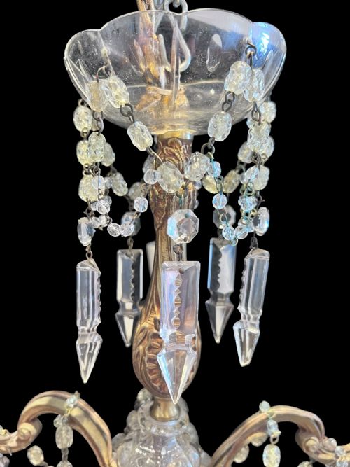 fig 1. A five-arm brass chandelier decorated with clear crystal drops, bead garlands, and white candle-style light sleeves.