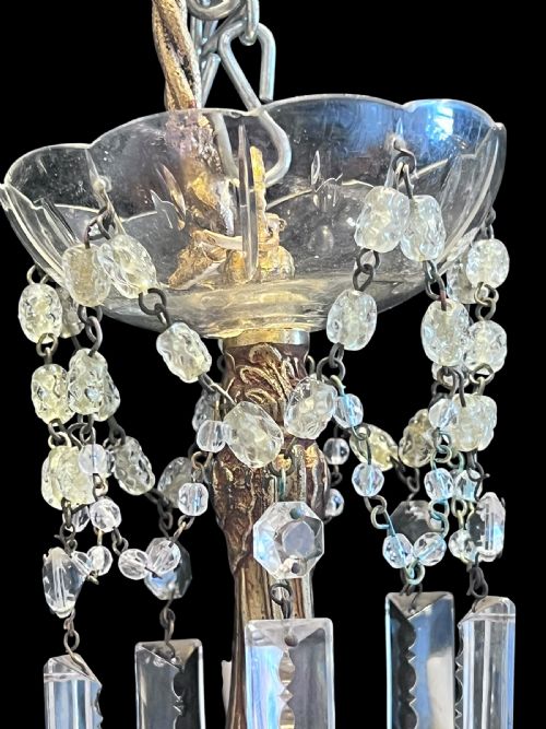fig 2. A five-arm brass chandelier decorated with clear crystal drops, bead garlands, and white candle-style light sleeves.