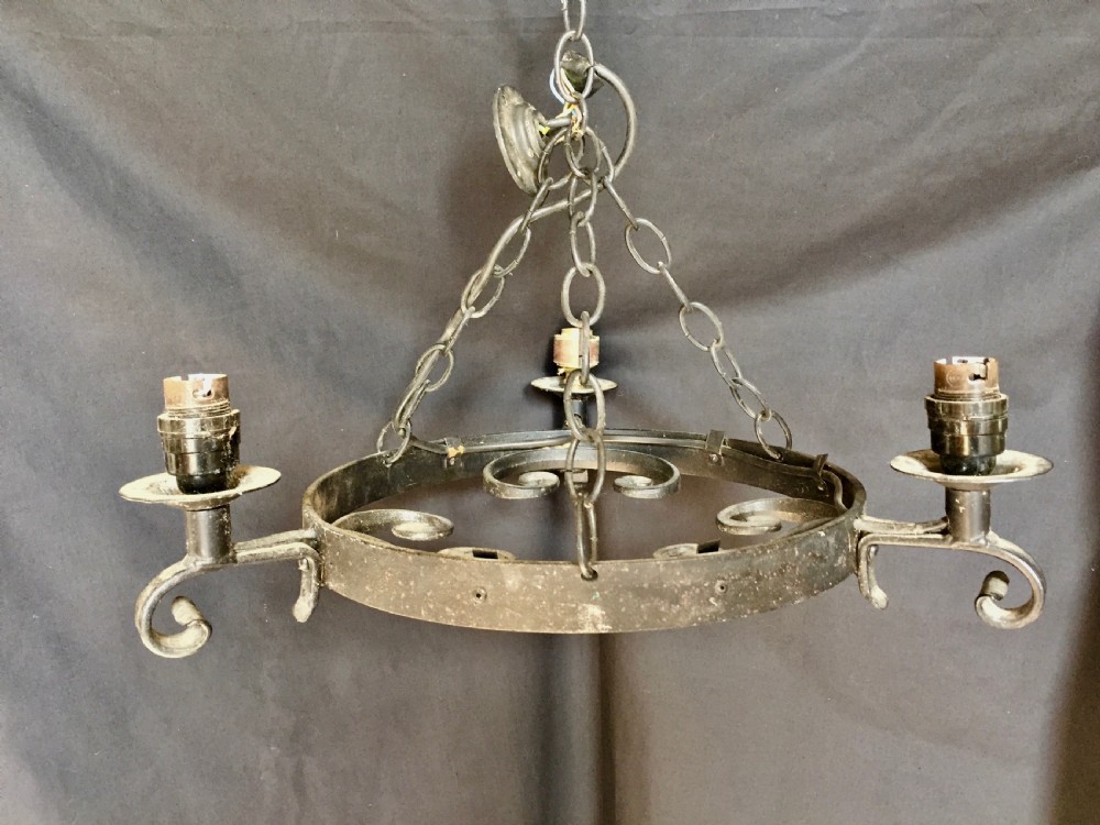 A three-light black wrought iron wagon wheel chandelier with scroll motifs, central suspension chains, and candle-style socket holders.