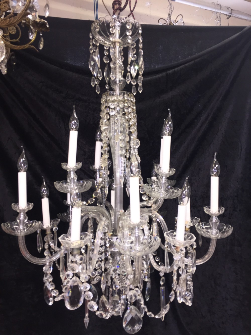 A multi-armed antique cut glass chandelier featuring cascading crystal drops, scalloped bobeches, and white candle sleeves.
