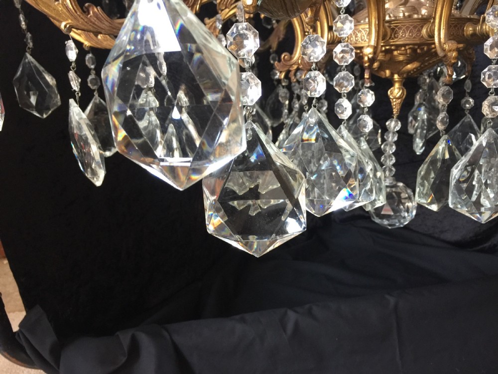 A large two-tiered brass chandelier featuring ornate scrolling arms, candle-effect sleeves, and clear faceted crystal droplets. View XIII