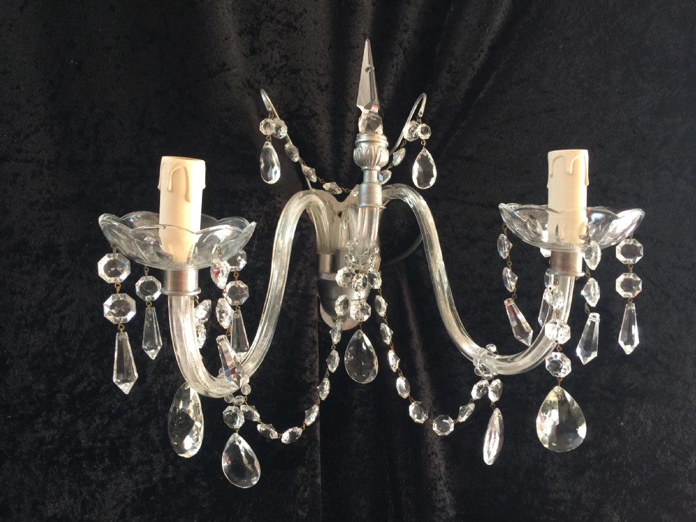 An English antique crystal wall light featuring two curved glass arms, scalloped drip pans with hanging faceted drops, and a central spire finial.