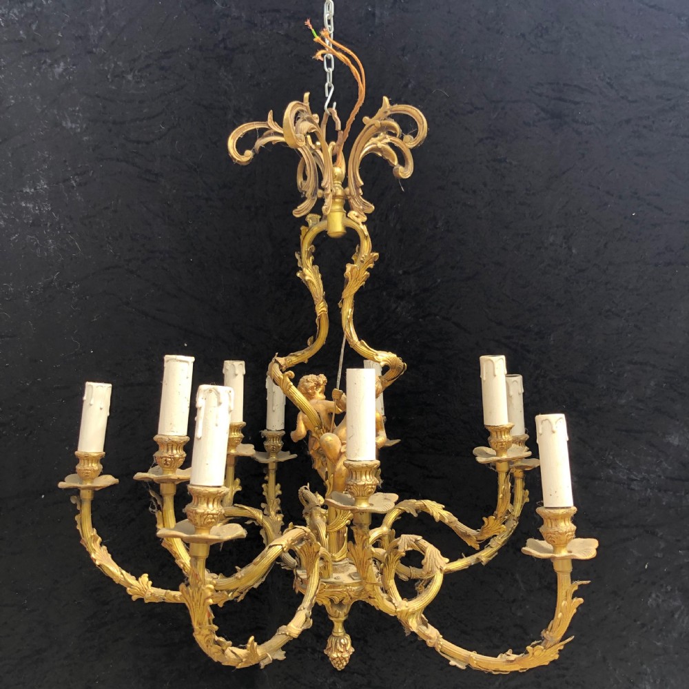 A French Rococo style ten-light gilt bronze chandelier featuring sculpted cherubs, scrolled acanthus leaf arms, and white candle sleeves.