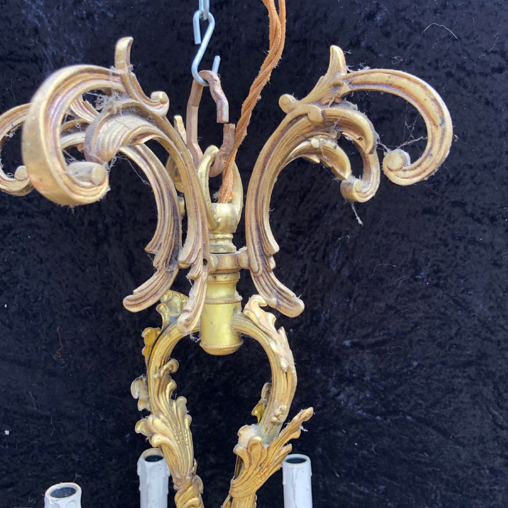 A French Rococo style ten-light gilt bronze chandelier featuring sculpted cherubs, scrolled acanthus leaf arms, and white candle sleeves. View II
