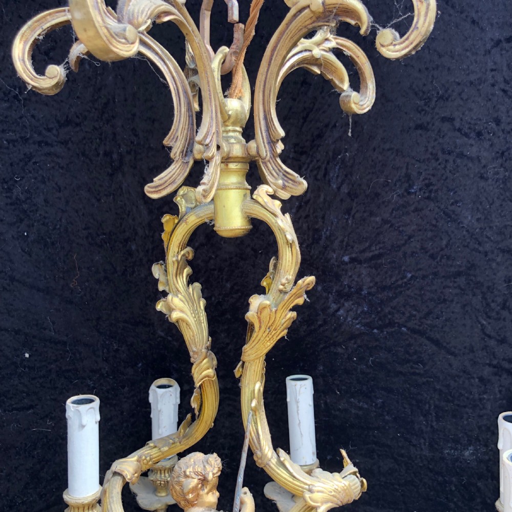 A French Rococo style ten-light gilt bronze chandelier featuring sculpted cherubs, scrolled acanthus leaf arms, and white candle sleeves. View III