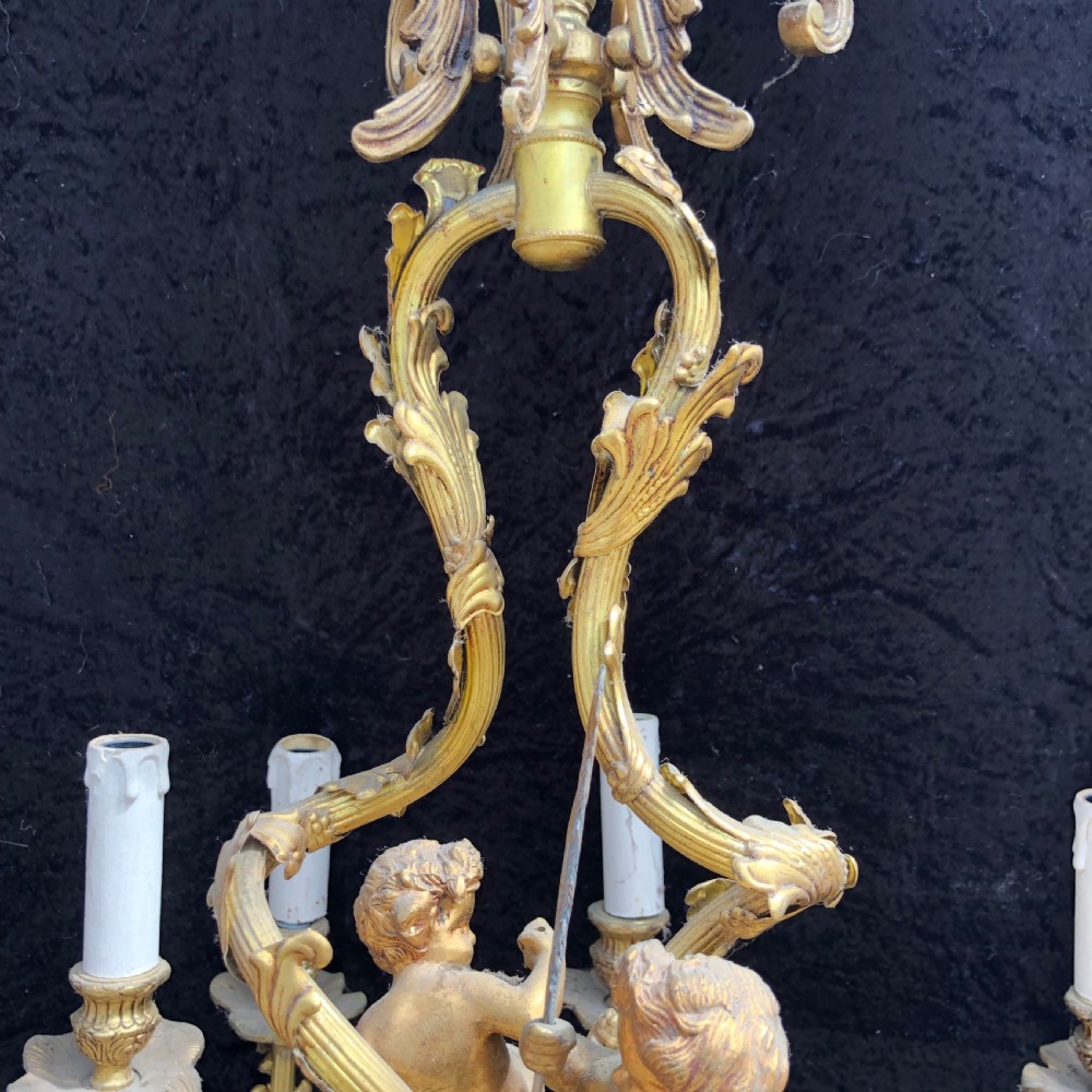 A French Rococo style ten-light gilt bronze chandelier featuring sculpted cherubs, scrolled acanthus leaf arms, and white candle sleeves. View IV