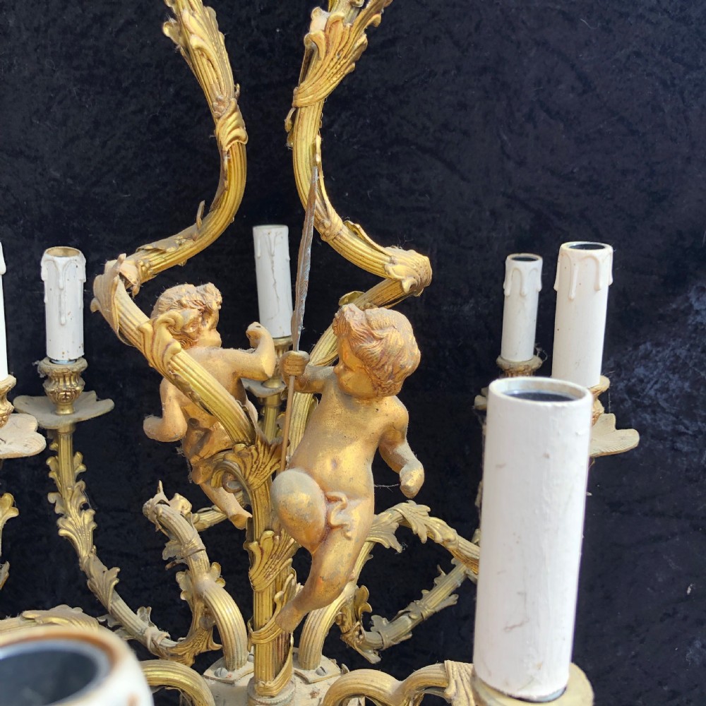 A French Rococo style ten-light gilt bronze chandelier featuring sculpted cherubs, scrolled acanthus leaf arms, and white candle sleeves. View V