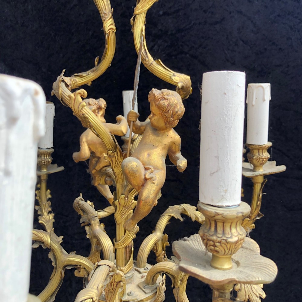 A French Rococo style ten-light gilt bronze chandelier featuring sculpted cherubs, scrolled acanthus leaf arms, and white candle sleeves. View VII
