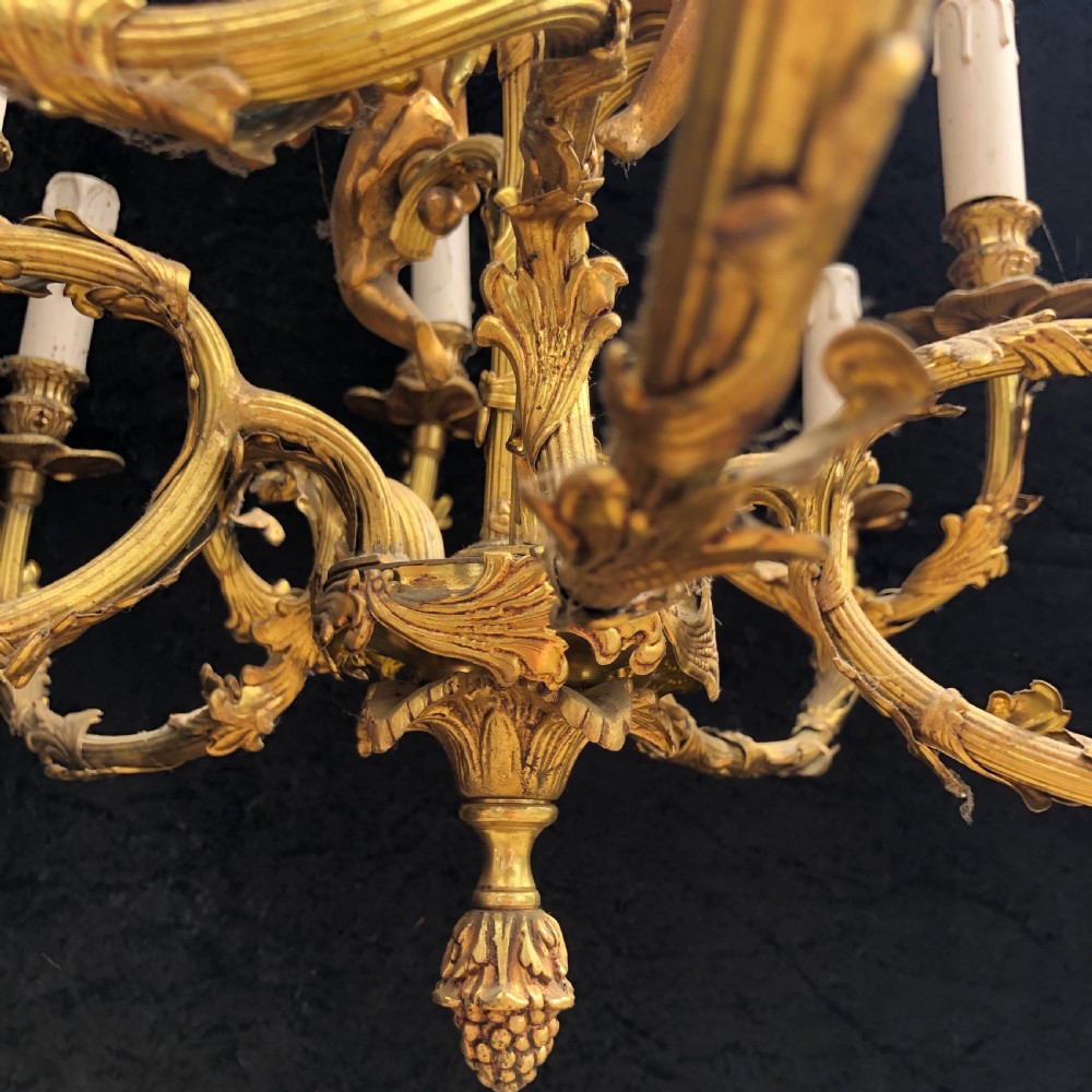 A French Rococo style ten-light gilt bronze chandelier featuring sculpted cherubs, scrolled acanthus leaf arms, and white candle sleeves. View IX