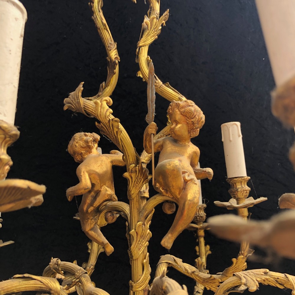 A French Rococo style ten-light gilt bronze chandelier featuring sculpted cherubs, scrolled acanthus leaf arms, and white candle sleeves. View X