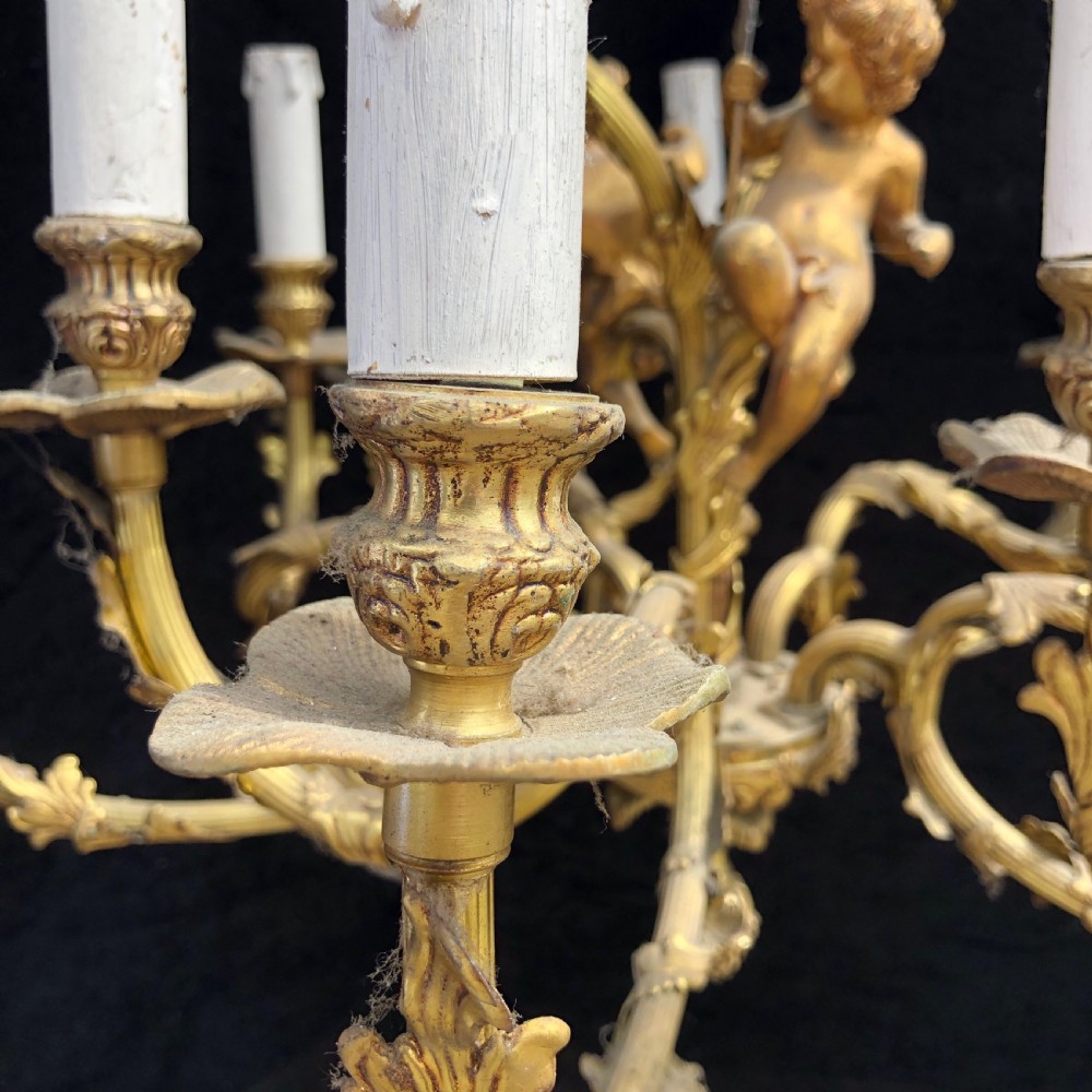 A French Rococo style ten-light gilt bronze chandelier featuring sculpted cherubs, scrolled acanthus leaf arms, and white candle sleeves. View XI
