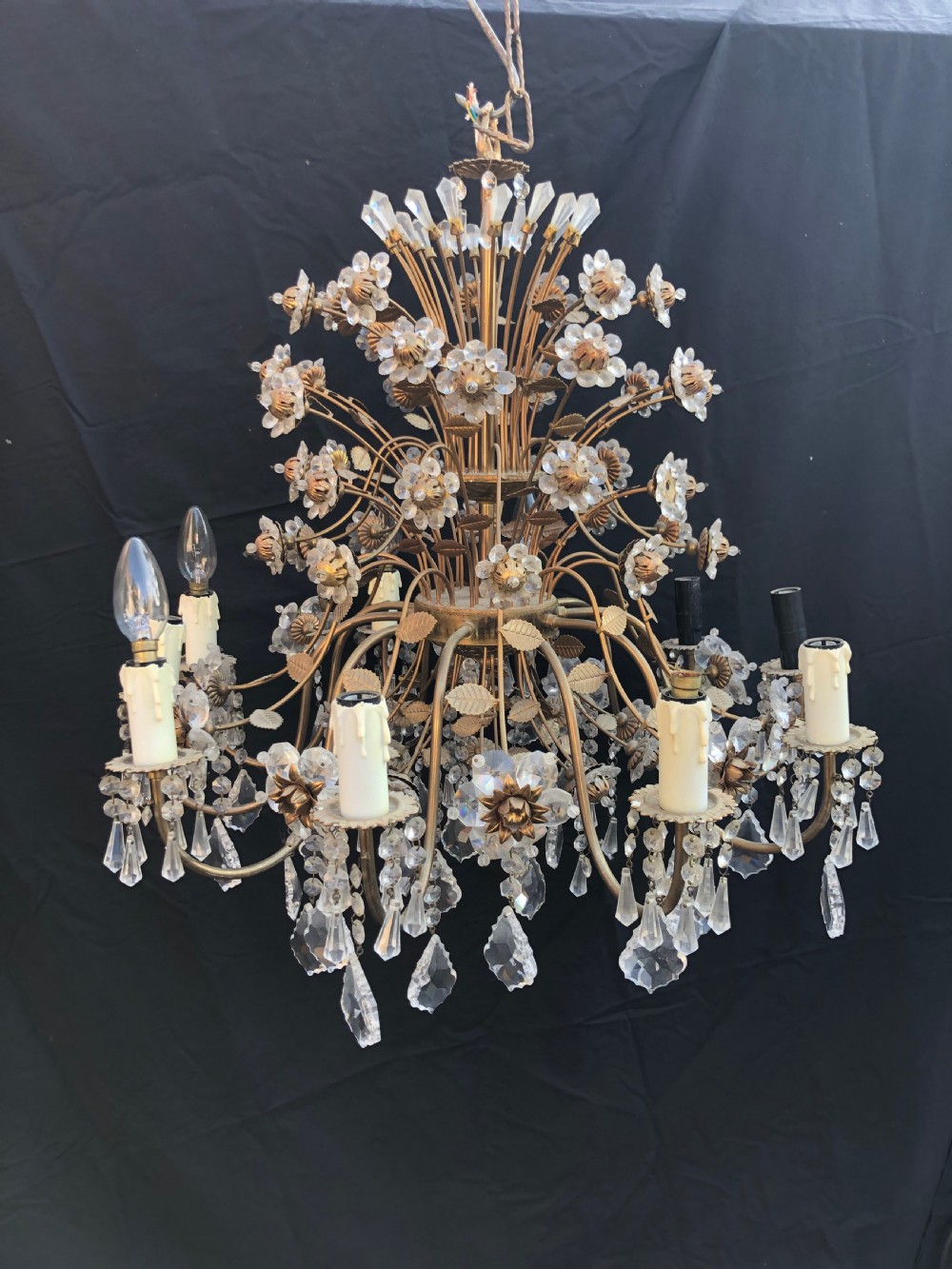 A twelve-light Florentine chandelier crafted from gilt metal featuring crystal flower heads, leaf details, and faceted crystal drops hanging from curved arms.
