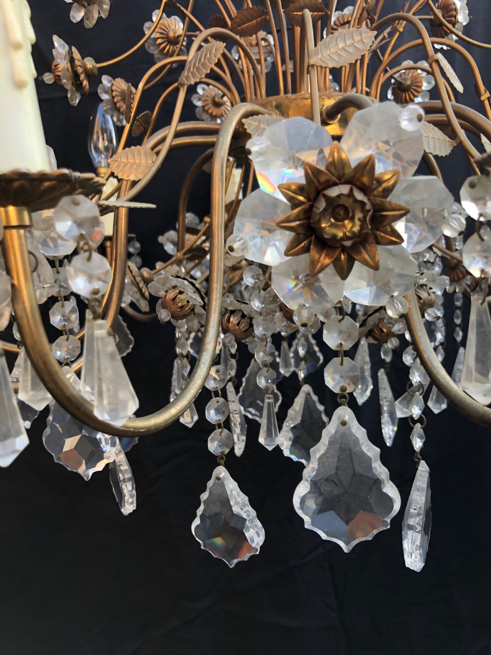 A twelve-light Florentine chandelier crafted from gilt metal featuring crystal flower heads, leaf details, and faceted crystal drops hanging from curved arms. View V