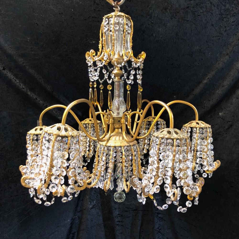 An Italian gilt-brass chandelier featuring multiple scrolling arms draped with crystal-beaded pod shades and amber glass drops.