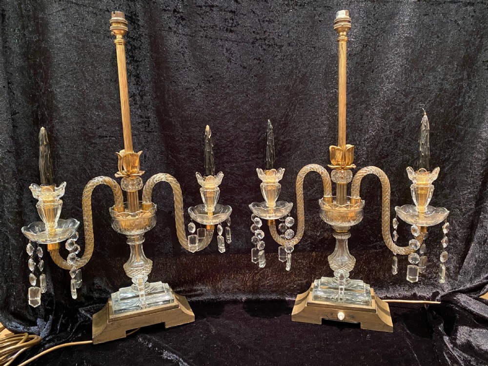 A pair of gilt brass and cut crystal two-arm candelabra table lamps featuring twisted glass arms, cascading crystal droplets, and stepped bases.