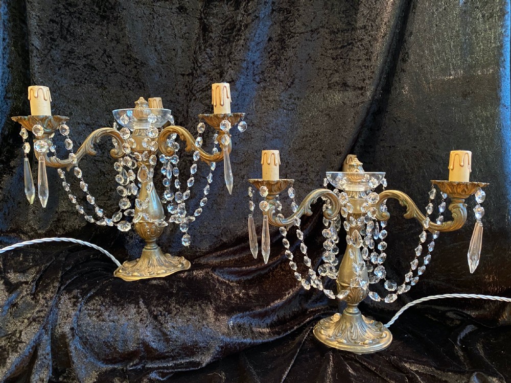 A pair of French gilt brass three-light candelabra table lamps adorned with hanging clear crystal prisms and beads.