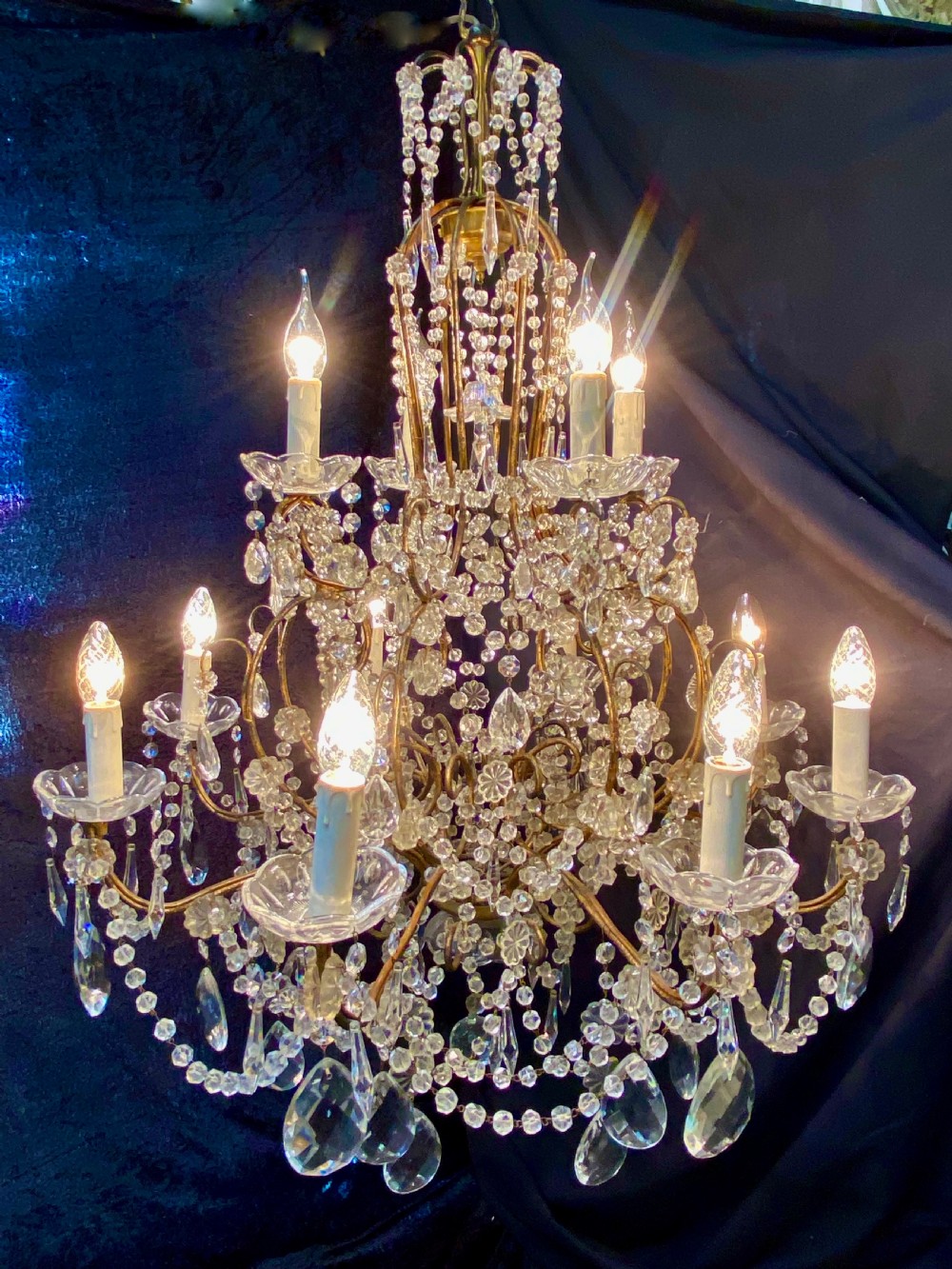 A twelve-light Florentine style chandelier featuring a gilded metal frame draped with clear faceted crystal beads and teardrop pendeloques.