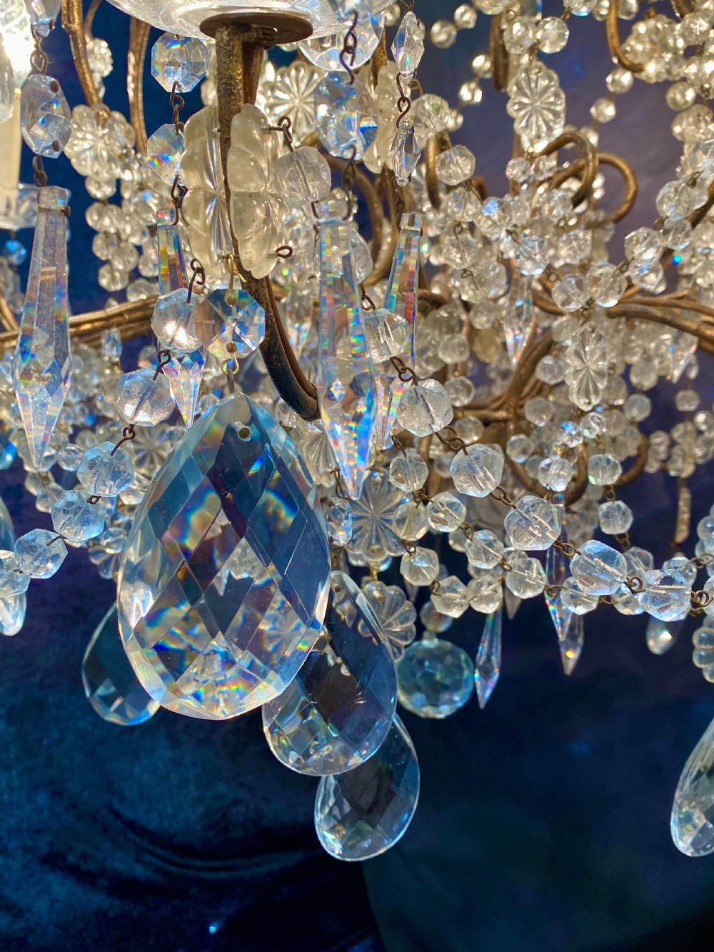 A twelve-light Florentine style chandelier featuring a gilded metal frame draped with clear faceted crystal beads and teardrop pendeloques. View V