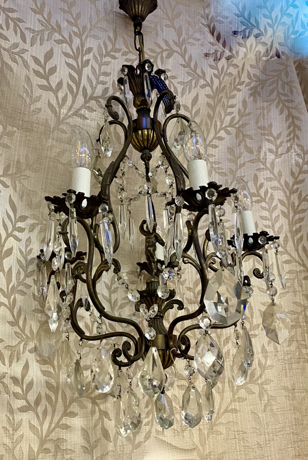 An Italian dark brass five-light chandelier adorned with crystal drops and a central metal cherub figurine.