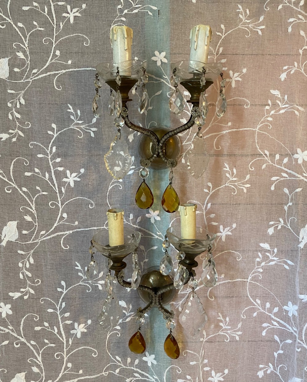 A pair of antique Florentine wall lights featuring twin curved metal arms wrapped in small glass beads, decorated with clear glass droplets, amber crystal prisms, and candle-style lamp holders.