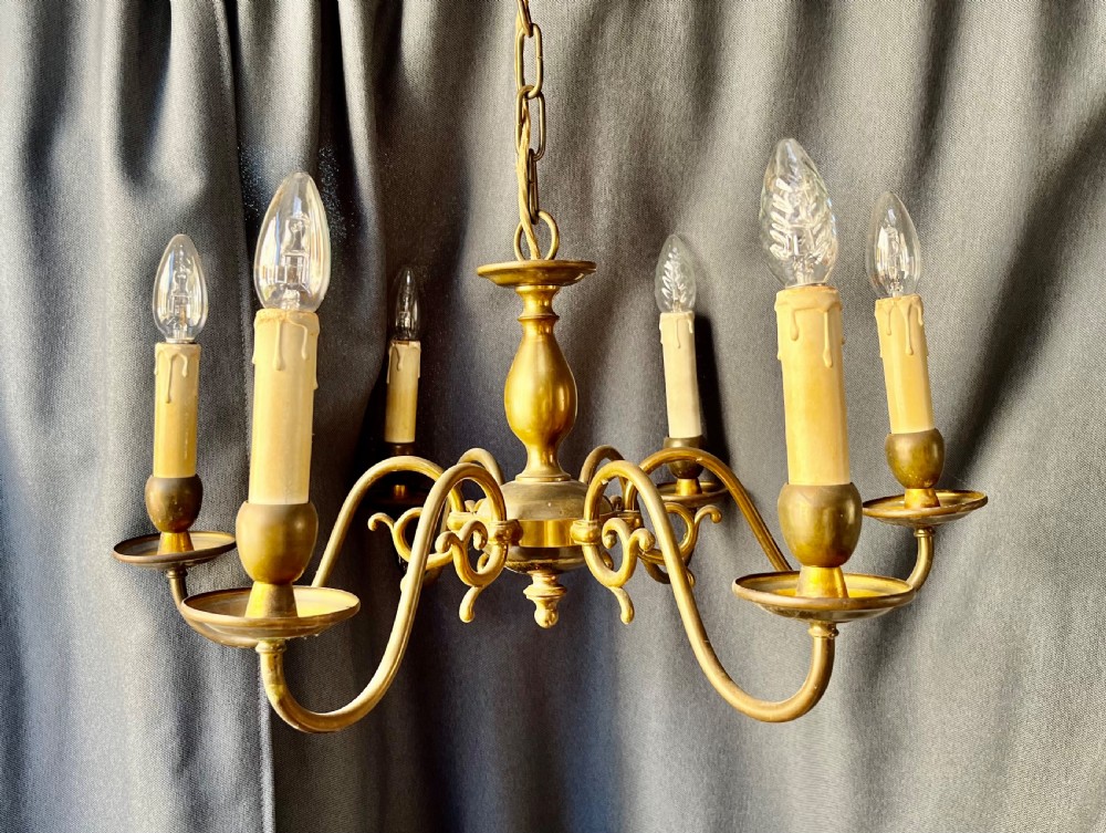 A six-arm brass Dutch pendant chandelier featuring a turned central baluster stem, scrolled arms, drip pans, and candle sleeves.