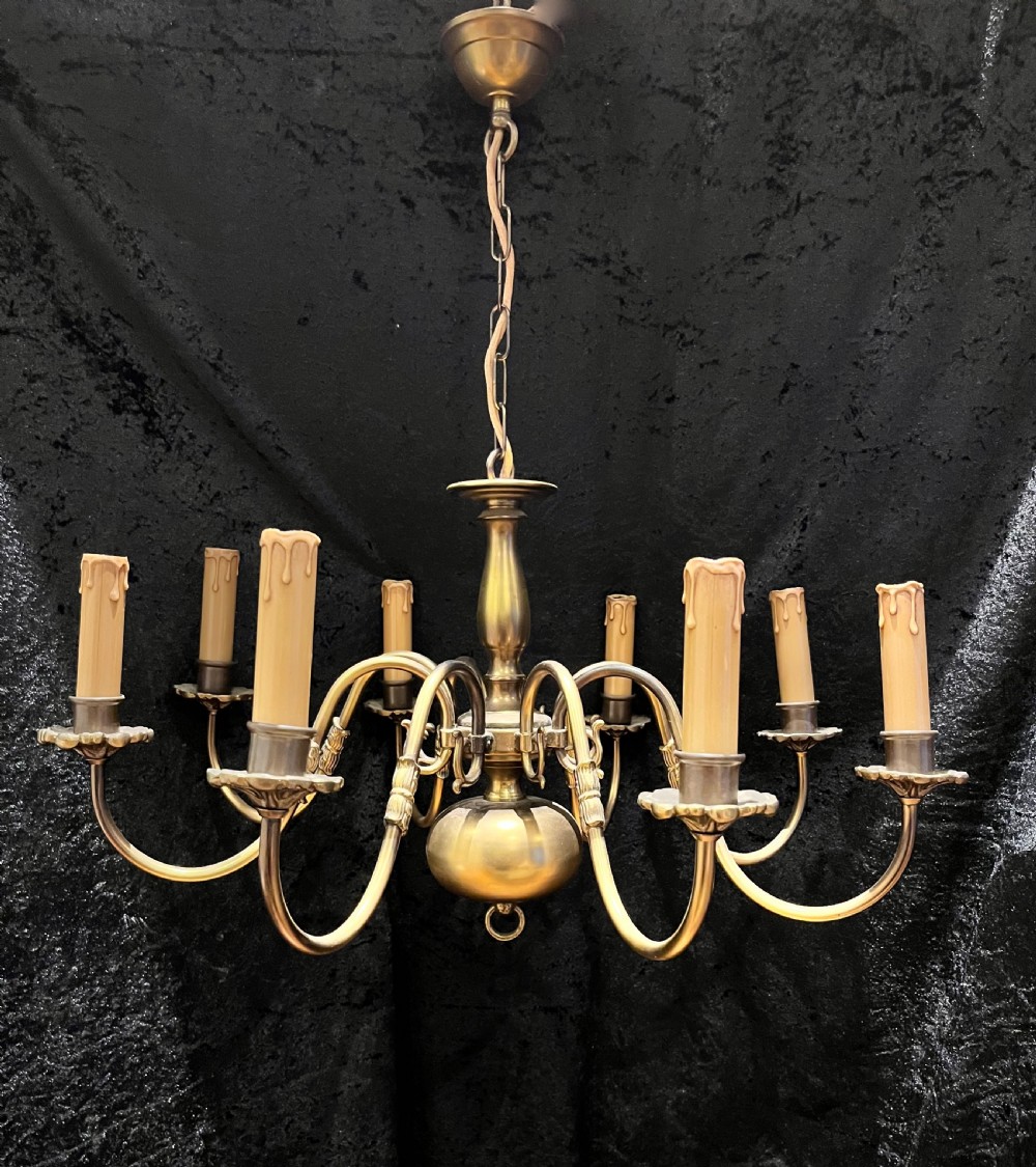 A 1920s Dutch brass eight-light chandelier featuring curved S-scroll arms with faux candle sleeves around a central turned baluster stem.