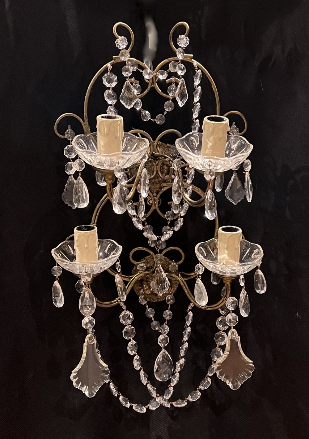 An Italian gilt metal four-light wall sconce adorned with cut crystal glass swags, drops, and faceted pendants.