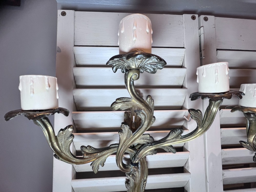 Pair of antique French gilded brass three-arm wall lights with foliate scrollwork and white candle sleeves. View III