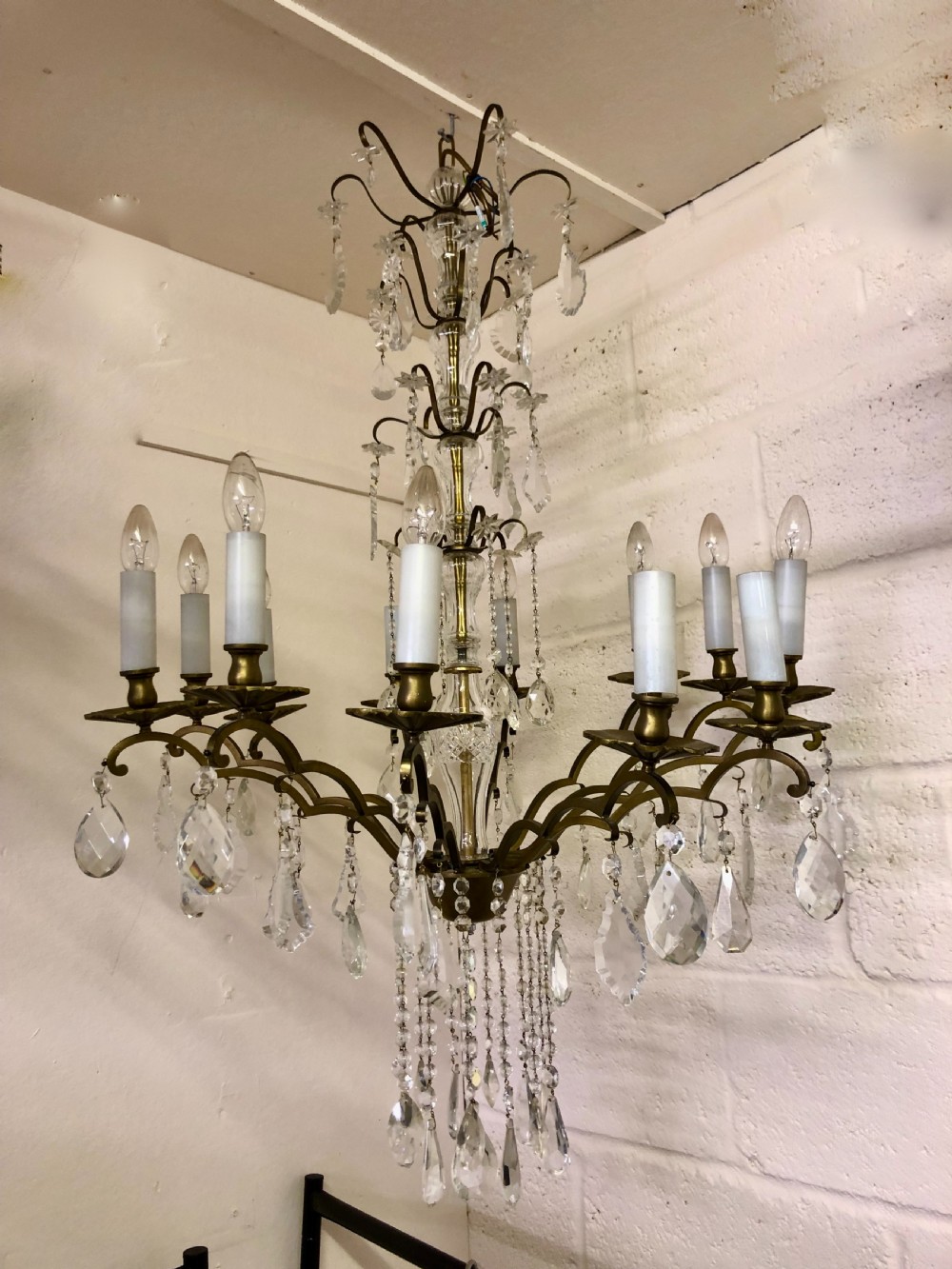 A twelve-light brass and crystal chandelier featuring curved brass arms, white faux candle sleeves, and suspended clear glass crystal prisms.