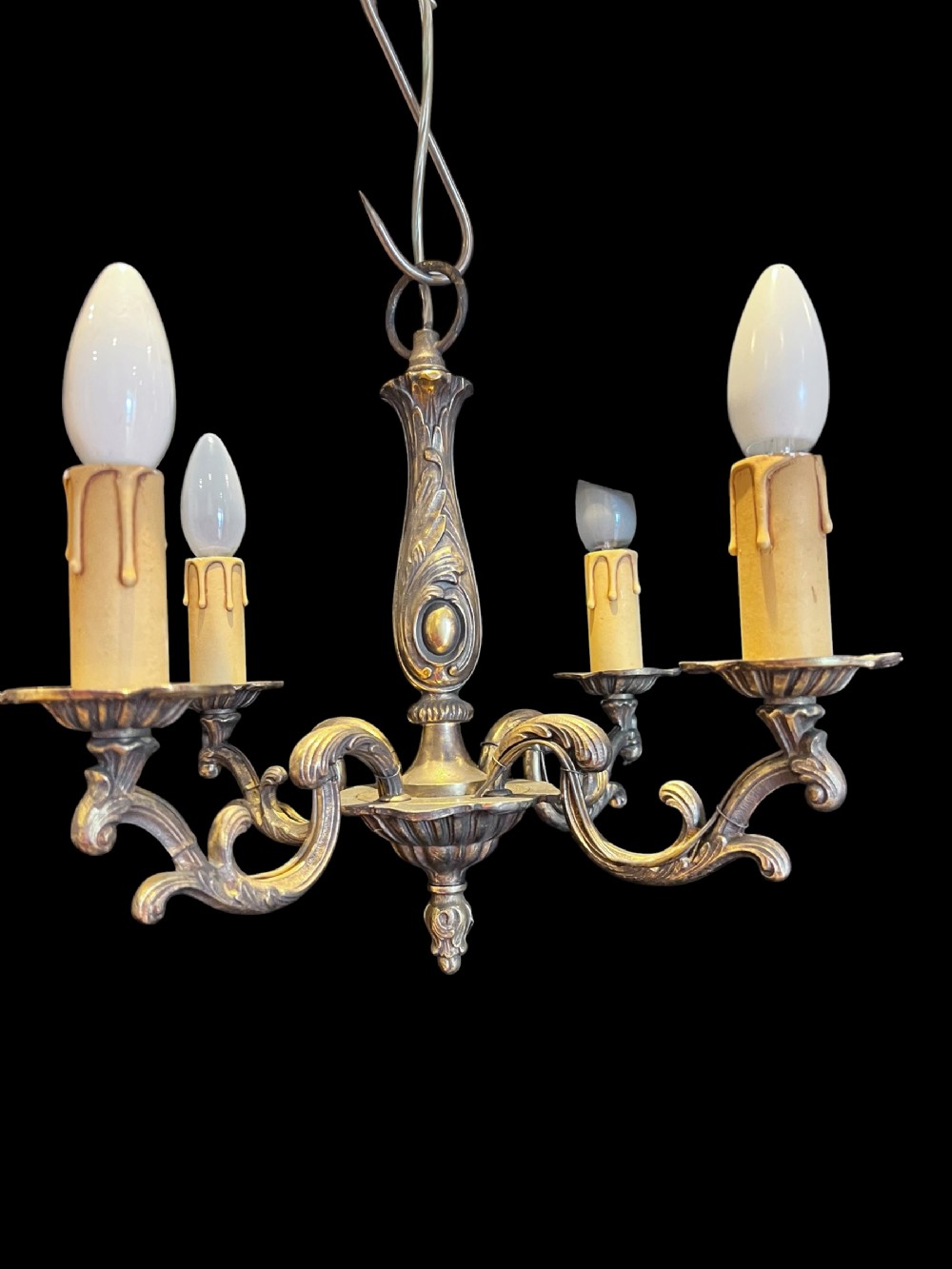 A four-light French antique brass pendant chandelier featuring ornate scrolling arms, cast embellishments, and faux candle sleeves.