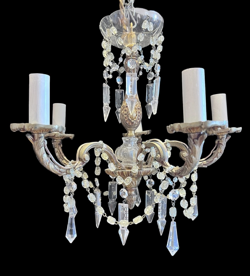 A five-arm brass chandelier decorated with clear crystal drops, bead garlands, and white candle-style light sleeves.