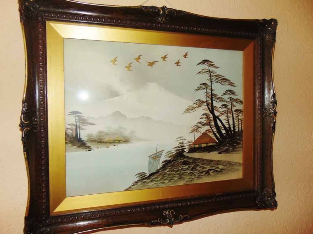 A framed Japanese embossed print depicting Mount Fuji, flying birds, pine trees, and a sailboat, enclosed in a dark carved wooden frame with a gold inner bevel.