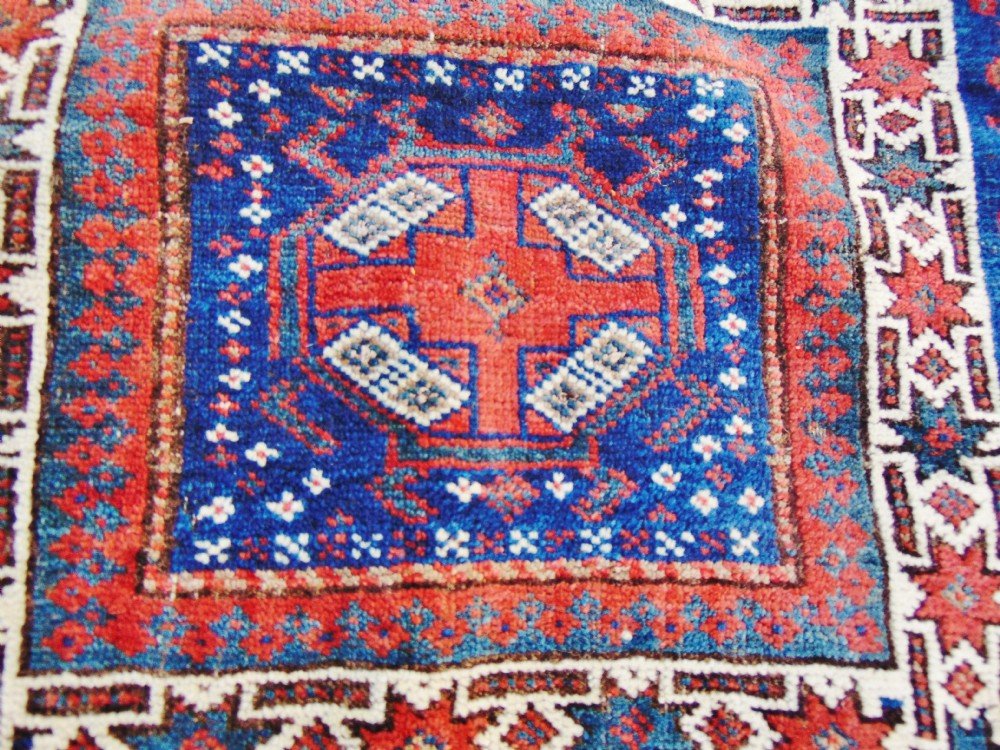 An antique square Baluch woven tribal bag face featuring geometric red, blue, and cream borders around a central medallion with wool side tassels. View II