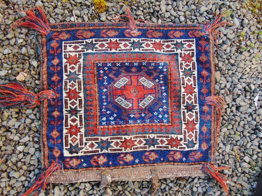 An antique square Baluch woven tribal bag face featuring geometric red, blue, and cream borders around a central medallion with wool side tassels.